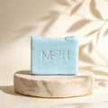Jabón artesanal Mayam Holistic Baño de Mar color azul claro sobre base de piedra con relieve de logo y aroma herbal